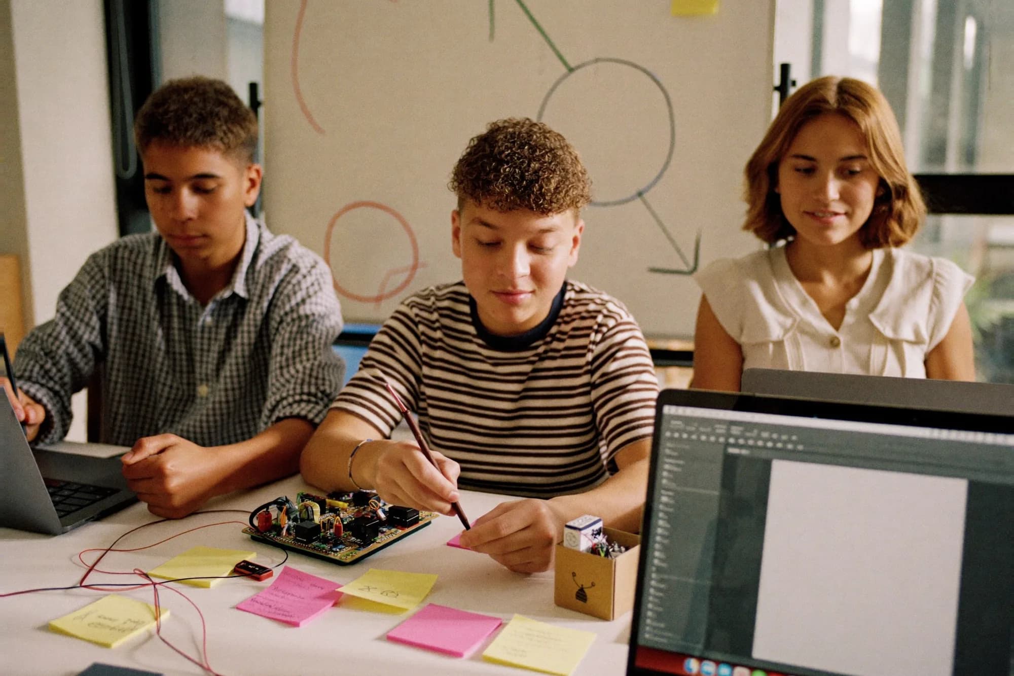 Young people working as a team at a table with sticky notes, electronics and laptops