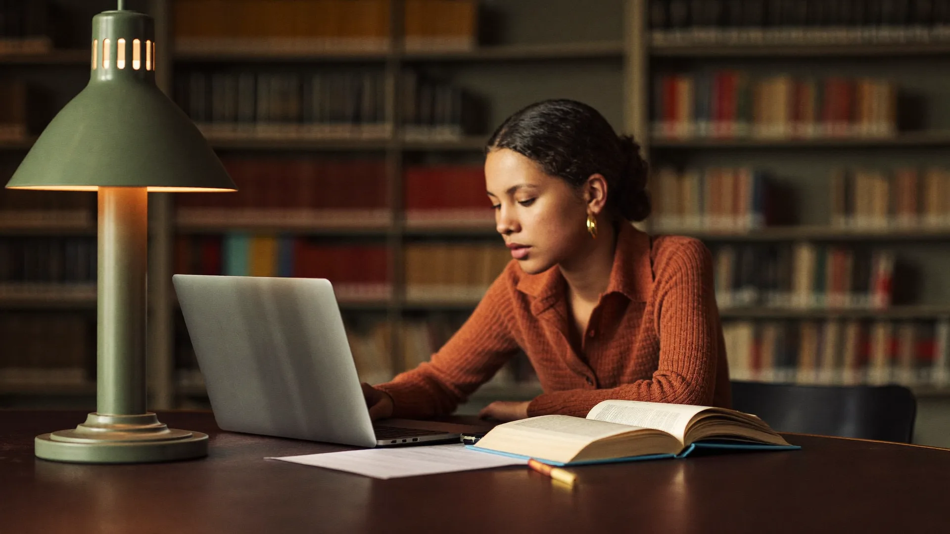 Focused student with a laptop and a book in a library